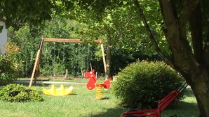 Ein Spielplatz mit Schaukeln, einer gelben Karussellbahn und einem roten Traktor.