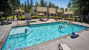 Une piscine entourée d’une clôture et d’arbres, avec des chaises longues et des parasols.