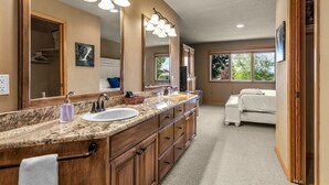 Une salle de bain avec une grande commode, un lavabo et un miroir. On aperçoit un lit au fond.