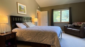 Quarto com cama, mesas de cabeceira, cômoda, janela com cortinas e porta.