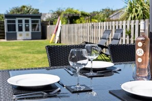 An outdoor dining table with two wine glasses, plates, and cutlery. A bottle of rosé wine is visible on the table.