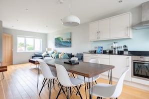 A modern kitchen with white cabinets, a wooden dining table, and a black countertop.