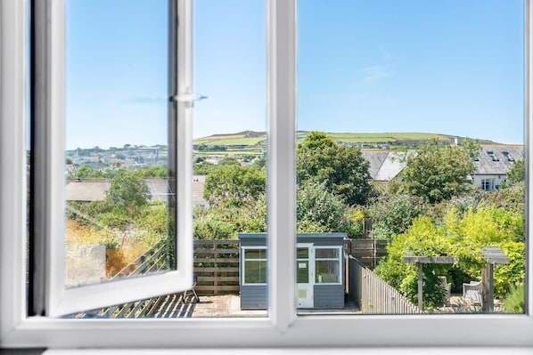 A view through a window of a residential area with a small shed, a wooden fence, and a garden.