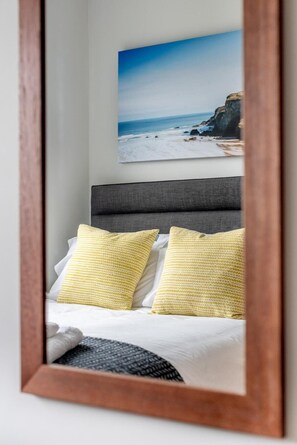 A bed with two yellow pillows, a grey headboard, and a framed picture of a beach scene on the wall above.