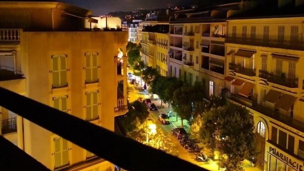 Une vue nocturne d’une rue de la ville, avec des immeubles, une pharmacie et la lune dans le ciel.