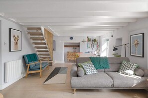 Una sala de estar moderna con una escalera, un conjunto de sofás, una estantería y un comedor.