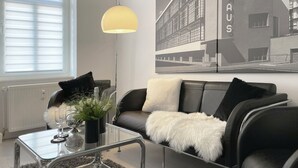 Una sala de estar moderna con una mesa de centro de vidrio, un sofá de cuero negro, un plaid blanco mullido y una lámpara de pie.