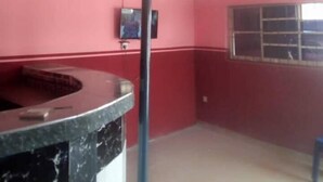 A room with a curved marble counter, a television mounted on the wall, and a window with a grid pattern. - Perfecto Hotel Suites Lounge (Ibadan)