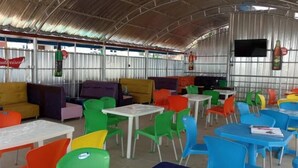 A covered outdoor seating area with colorful plastic chairs and tables, a Budweiser sign, and a television screen mounted on the wall. - Perfecto Hotel Suites Lounge (Ibadan)
