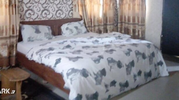 A bedroom with a patterned wallpaper, a bed with a patterned duvet, and curtains. - Perfecto Hotel Suites Lounge (Ibadan)