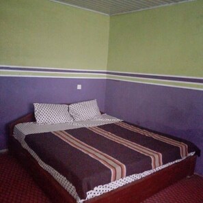 A single bed with a patterned bedspread and pillows, a wooden headboard, and a red carpeted floor. - Perfecto Hotel Suites Lounge (Ibadan)