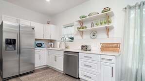 Una cocina moderna con armarios blancos, refrigerador de acero inoxidable, microondas, lavavajillas y encimera de madera.