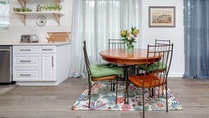 Un comedor con una mesa redonda de madera, sillas tapizadas de color verde y un suelo de alfombra con motivos florales.