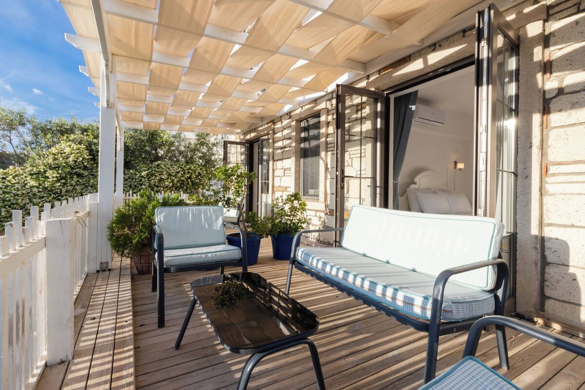 A wooden deck with a white fence, two blue cushioned chairs, a small table, and potted plants.