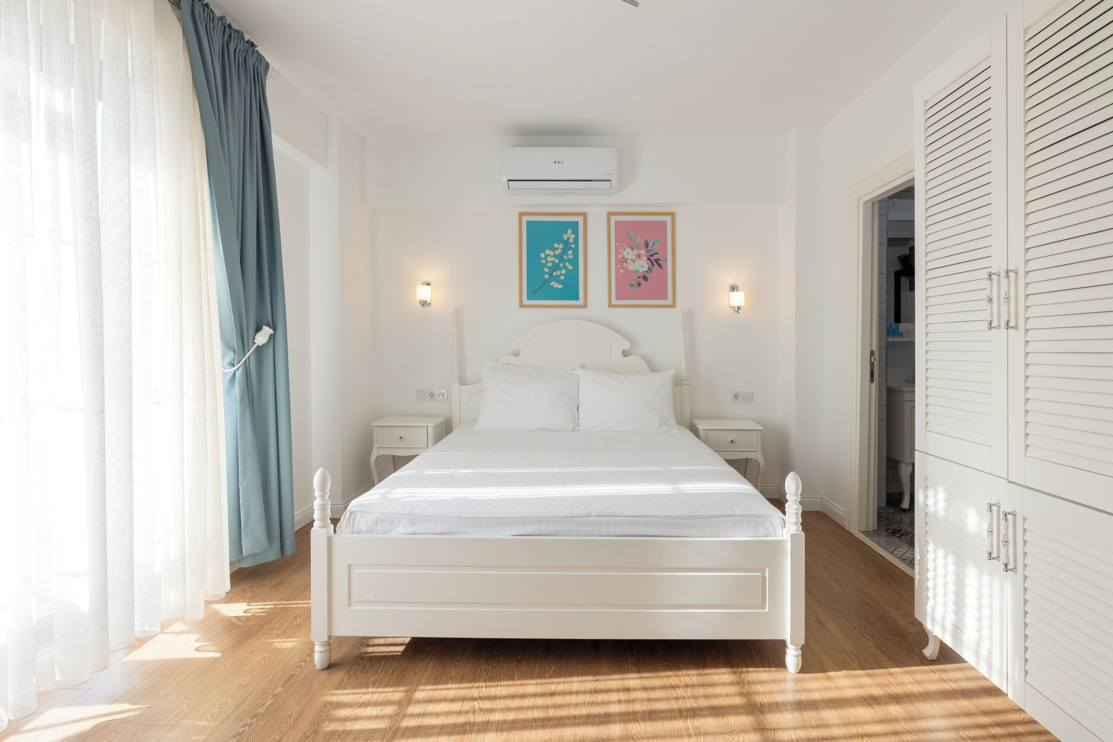 Un dormitorio con una cama blanca, suelo de madera y un armario.