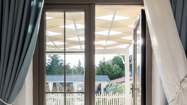A room with a sliding glass door leading to an outdoor deck with a wooden floor and a white fence. - Fitoz Otel (Bozcaada)