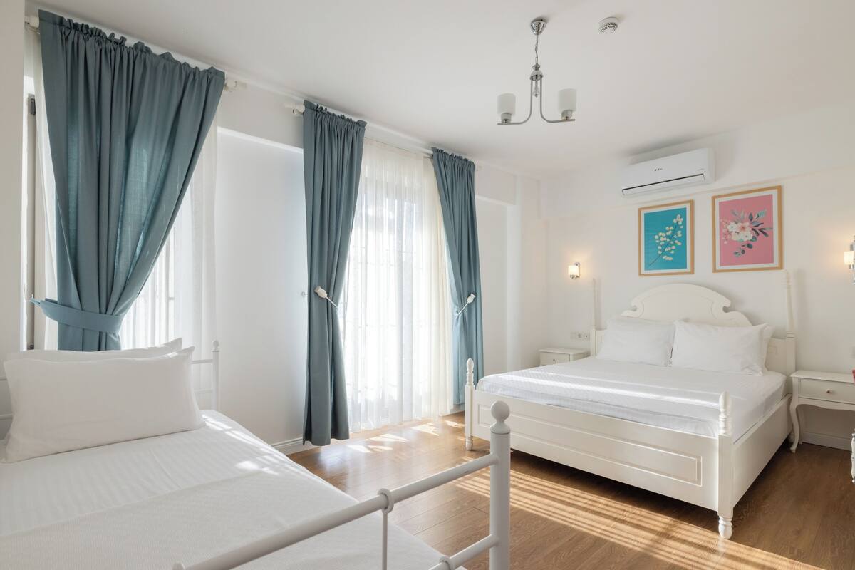 A bedroom with two beds, a white air conditioner, and two wall-mounted light fixtures.