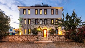 A two-story building with a stone facade, multiple windows, and a red door. - Fitoz Otel (Bozcaada)