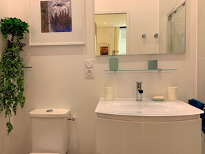 A bathroom with a toilet, sink, and mirror. There is a framed artwork above the mirror and a plant on the left. - Art Studio 2: Charm, Comfort, and Design in the Historic Center (La Rochelle)