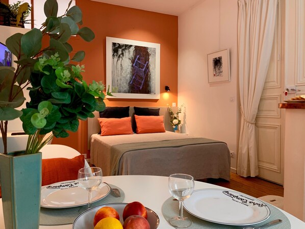 A hotel room with a bed, a painting on the wall, a dining table with plates and glasses, and a plant. - Art Studio 2: Charm, Comfort, and Design in the Historic Center (La Rochelle)