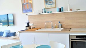 A modern kitchen with a built-in oven, a coffee maker, and a sink. There is a dining table with blue plates and wine glasses. - Air-conditioned 1BR apartment with parking in Cavalaire-sur-Mer (Cavalaire-sur-Mer)