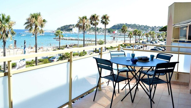 A balcony with a table and chairs overlooking a beach with palm trees and boats. - Air-conditioned 1BR apartment with parking in Cavalaire-sur-Mer (Cavalaire-sur-Mer)
