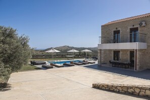 A building with a stone facade, a pool with lounge chairs, and a view of mountains.
