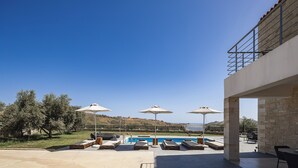 Area piscina con lettini e ombrelloni, un edificio in pietra e vista sulle colline.