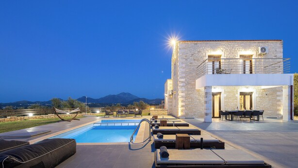 Area piscina con sedie a sdraio, un tavolo da pranzo e un edificio in pietra con un balcone.