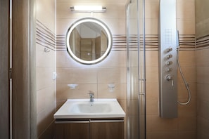 A bathroom with a sink, mirror, shower, and tiled walls.