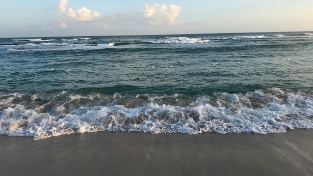 A beach with waves crashing onto the shore under a partly cloudy sky.