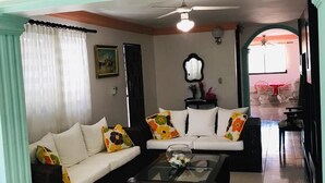 A living room with a sofa set, a coffee table, and a dining area visible in the background.