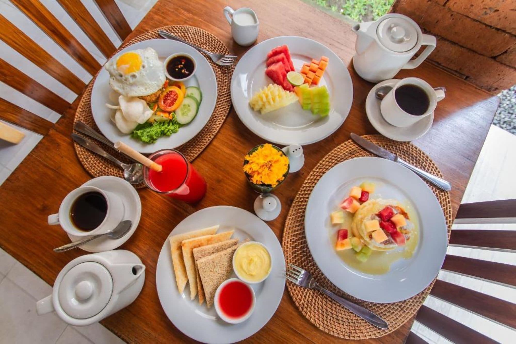 A breakfast setting with plates of food, cups of coffee, and a teapot on a wooden table.