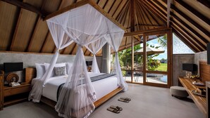 A bedroom with a canopy bed, wooden headboard, bedside tables with lamps, a view of a garden through large windows, and a wooden floor. - Lasamana Villas Ubud by GenuineHost (Ubud)