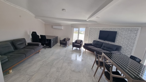 Un amplio salón con sofá, sillones, mesa de comedor y televisor montado en la pared.