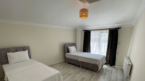 Un dormitorio con dos camas, un ventanal con cortinas y una lámpara colgante.