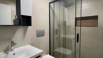 A modern bathroom with a white sink, a toilet, a glass shower enclosure, and a ceiling light.