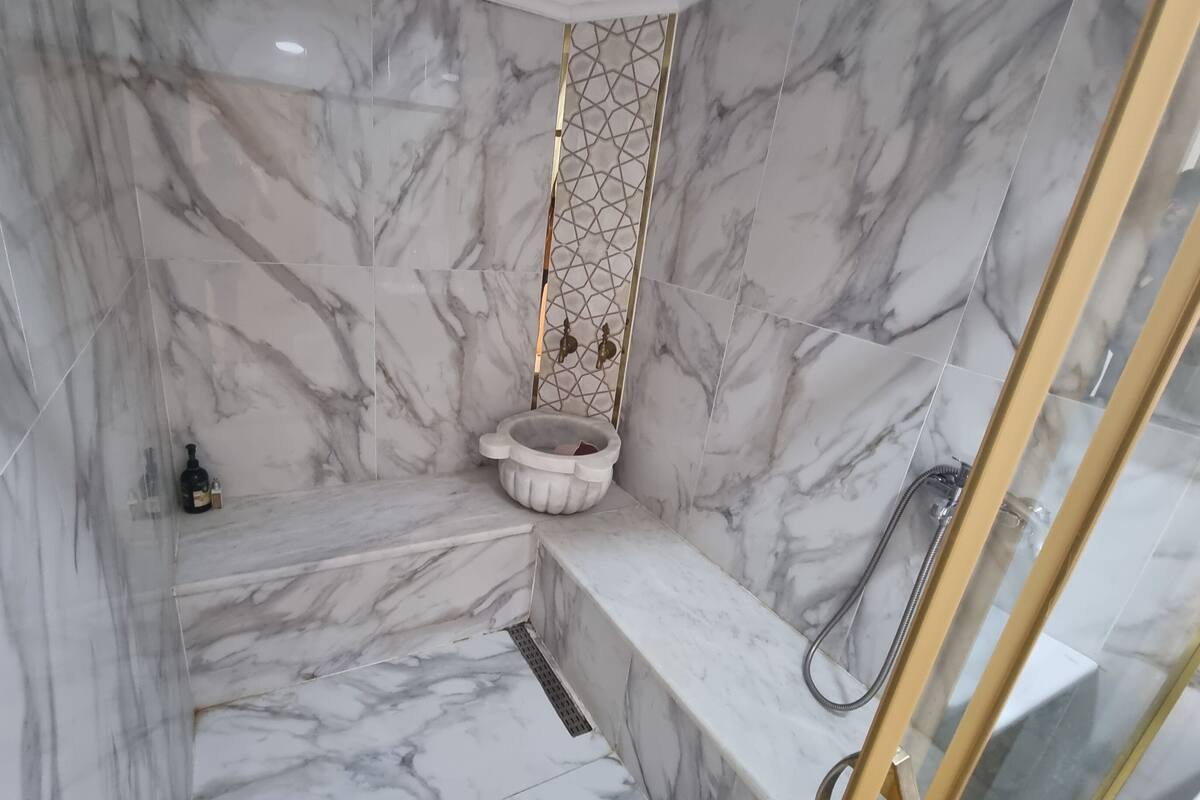 Ein Badezimmer mit Marmor, ausgestattet mit einer Duschkabine, einem Waschbecken und einer Toilette.