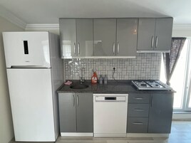 Una cocina moderna con armarios grises, un lavavajillas blanco y una estufa de acero inoxidable.