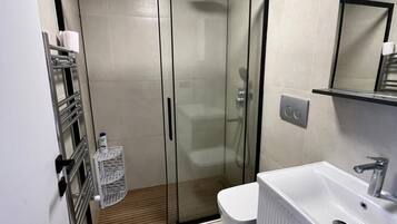 Ein modernes Badezimmer mit einer gläsernen Duschkabine, einem weißen Waschbecken mit Spiegel darüber und einer Toilette.
