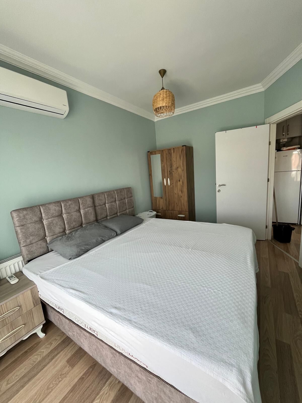 Un dormitorio con cama, armario, espejo y lámpara colgante.