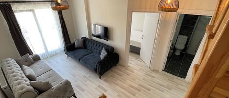 A modern living room with a sofa, a television, and a wooden staircase.