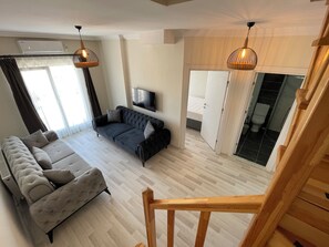 A modern living room with a sofa, a television, and a wooden staircase.