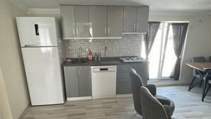 Una cocina moderna con gabinetes grises, un refrigerador blanco y un lavavajillas. Hay un comedor con una mesa y sillas.