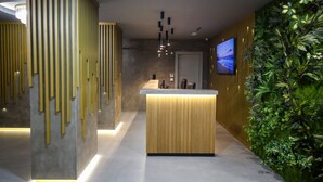 Un espace d’accueil moderne avec un comptoir de réception en bois, un téléviseur à écran plat et un mur végétal.