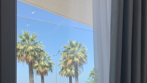 Une fenêtre donnant sur une plage, des palmiers et un ciel dégagé.