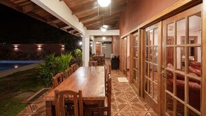 Un área de comedor al aire libre con una larga mesa de madera y sillas, rodeada por un patio empedrado.
