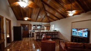 Amplia sala de estar con una cocina al fondo, un sofá de cuero y una televisión.