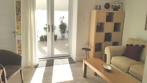 Olohuoneessa on sohva, sohvapöytä, puinen kaappi ja ovi, joka johtaa parvekkeelle, jossa on kasveja.