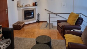 Un salon avec une cheminée, un téléviseur fixé au mur, un canapé avec des coussins et une table basse.